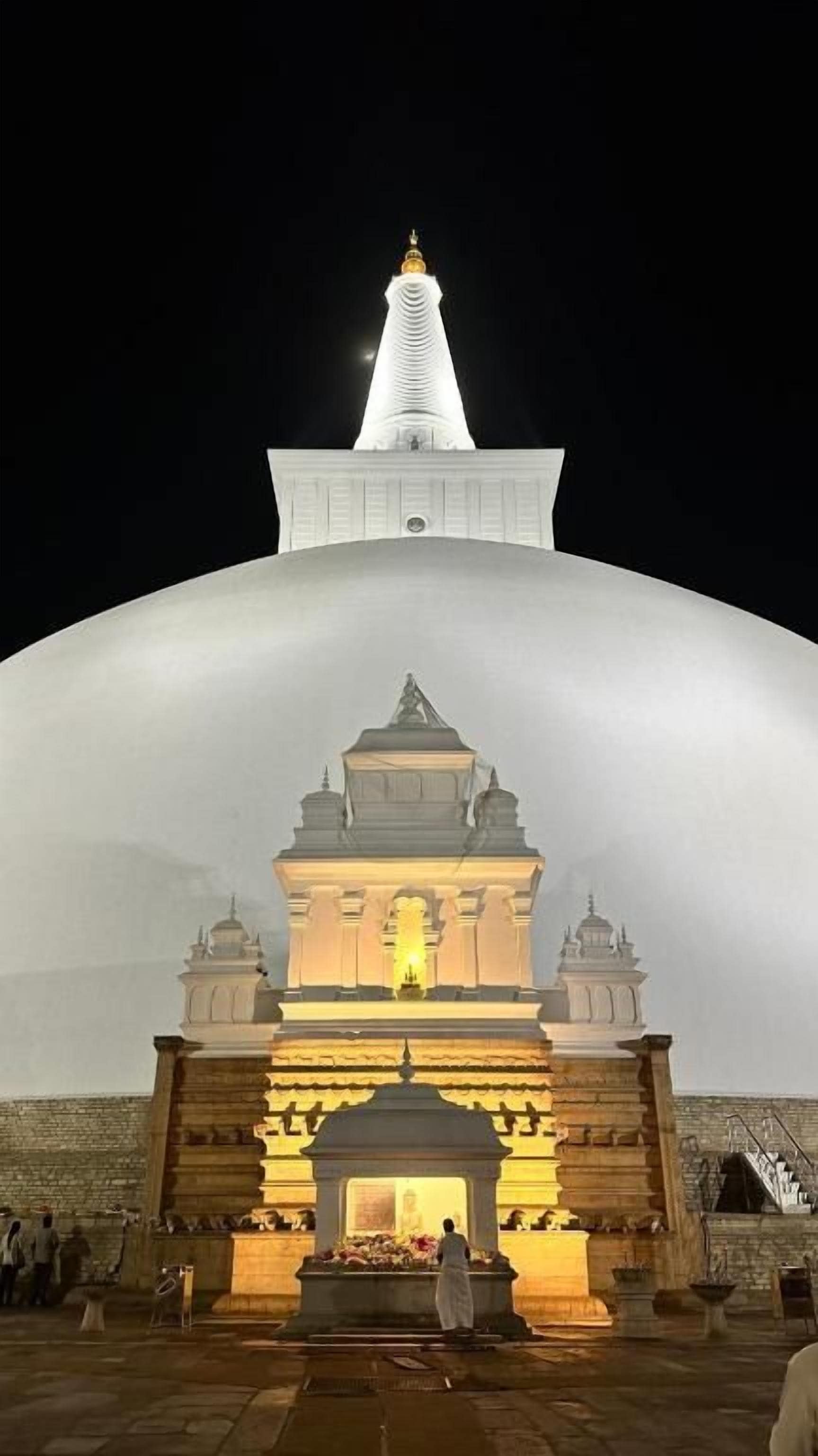 Una gran estructura en forma de cúpula blanca con un pequeño santuario iluminado en su base.