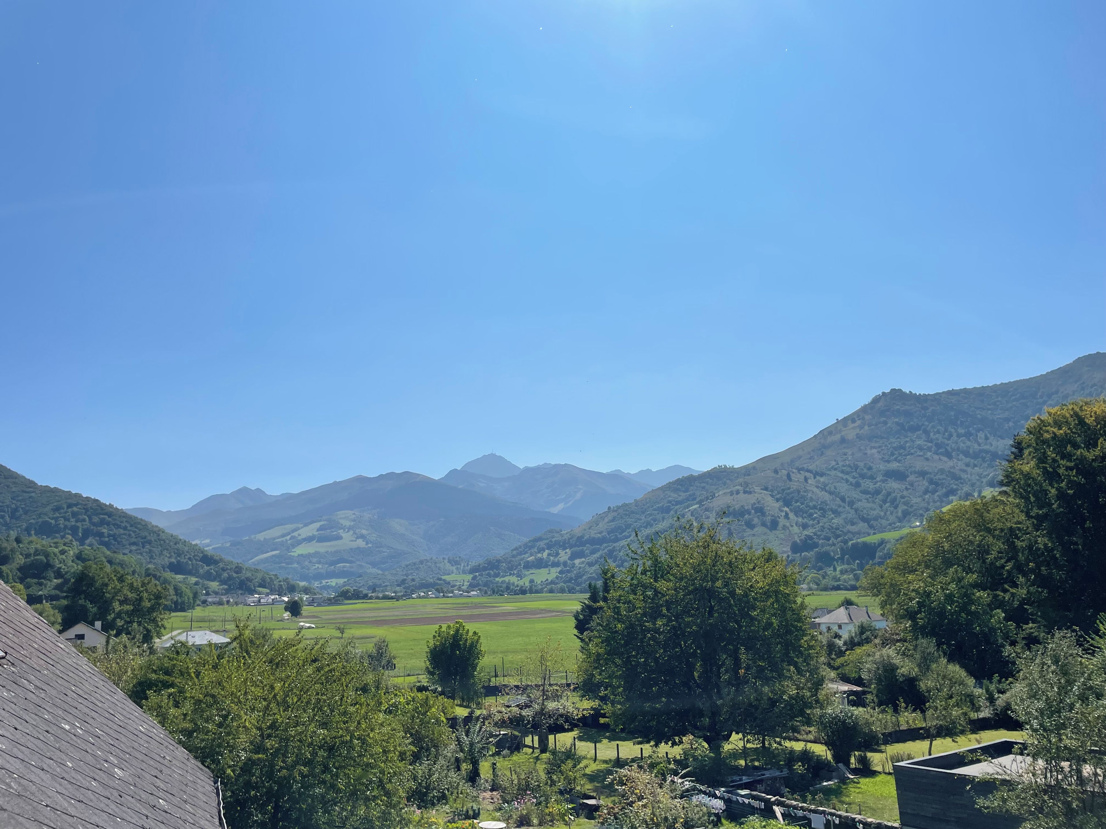 Un paisaje rural con montañas, cielo despejado y una casa con tejado inclinado.