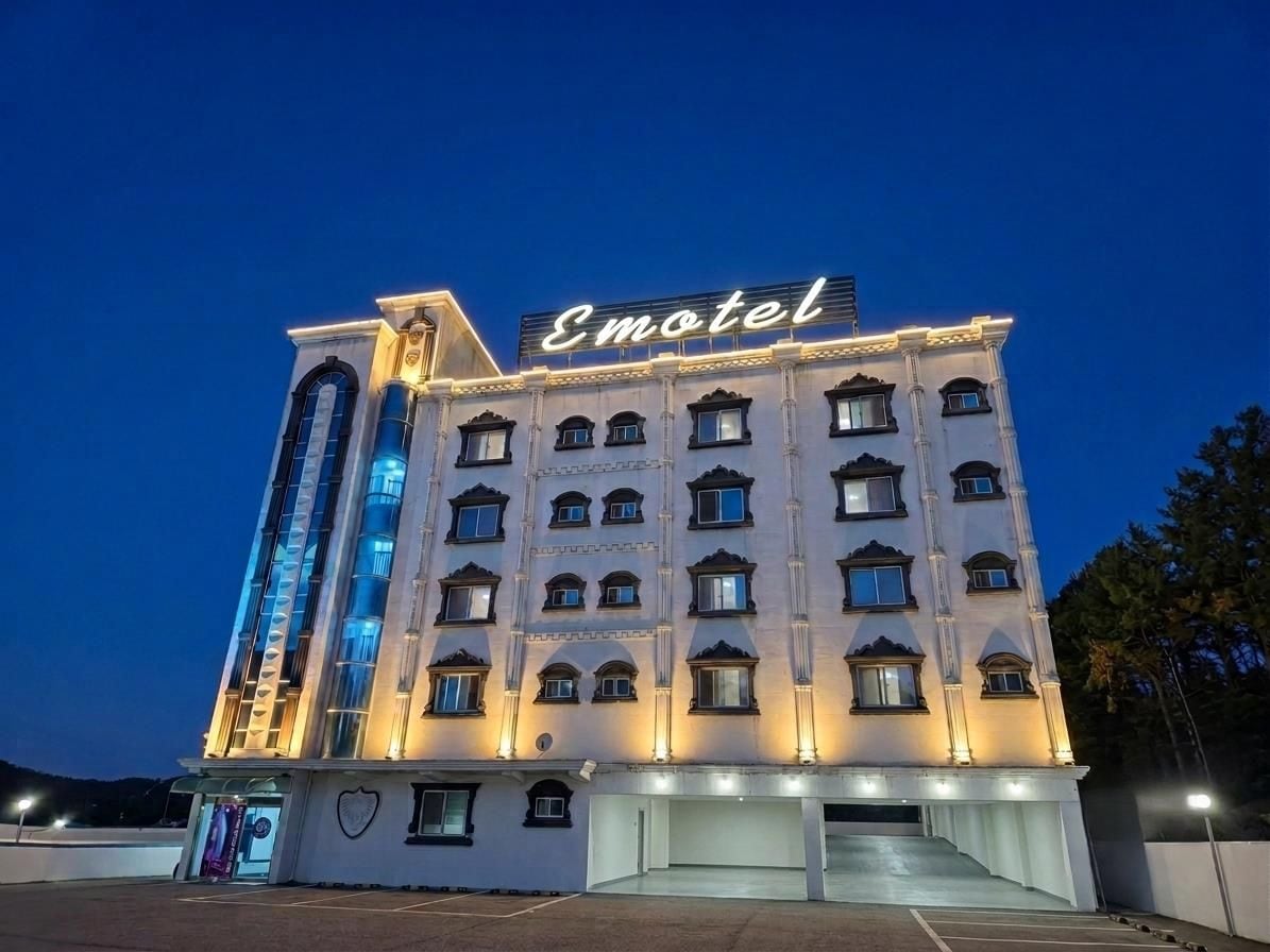 Un motel de varios pisos con un llamativo letrero de neón, un estacionamiento y una entrada amplia.
