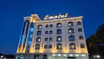 Un motel de varios pisos con un llamativo letrero de neón, un estacionamiento y una entrada amplia.