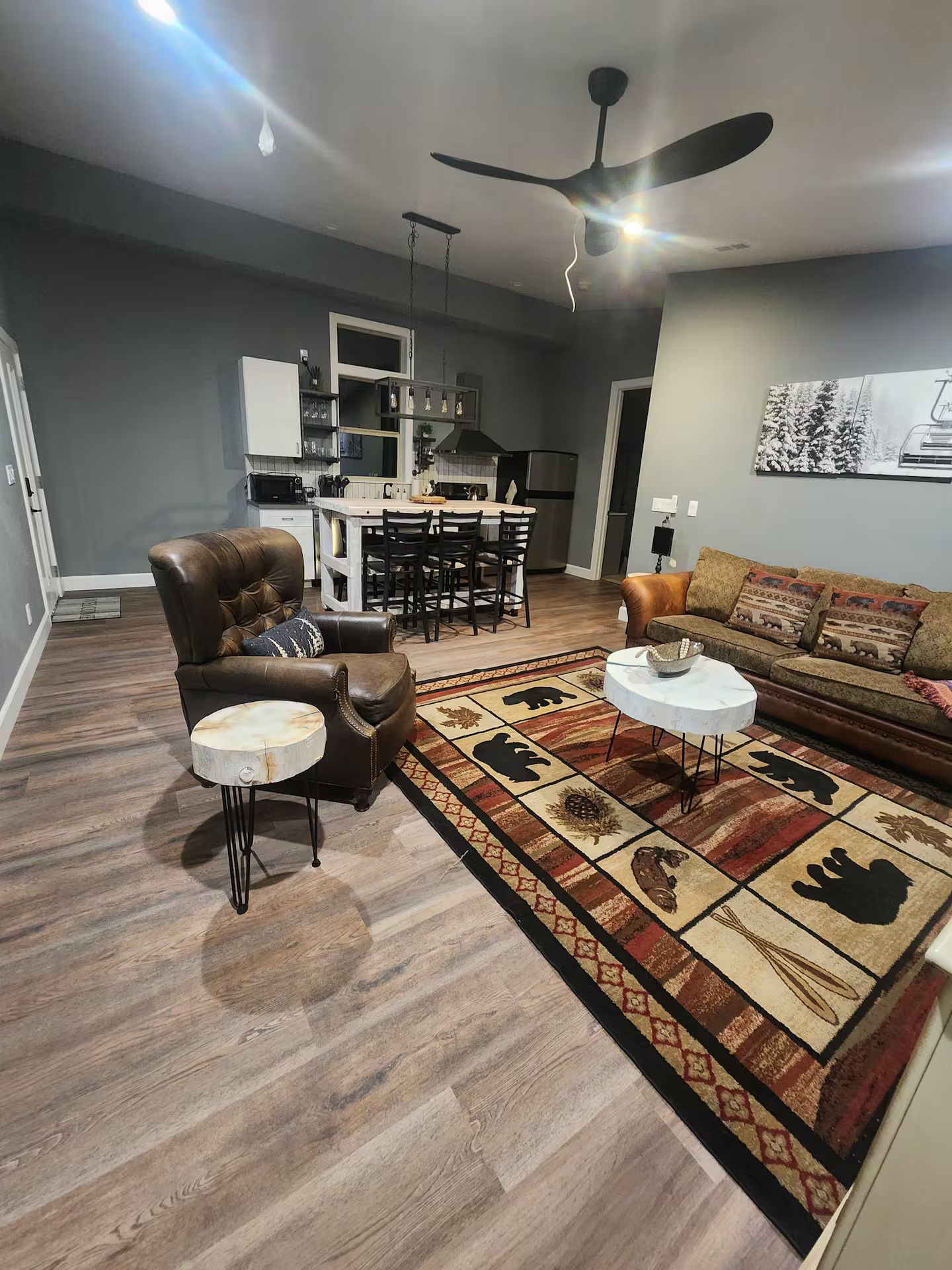A modern living room with a brown leather sofa, a patterned rug, and a dining area with a bar.