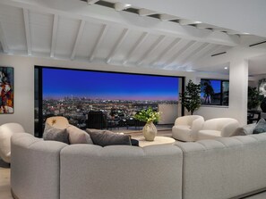 A modern living room with a large window, grey sofas, and a city view. - Maravilla Mirador By Alora Reserve (Los Angeles)