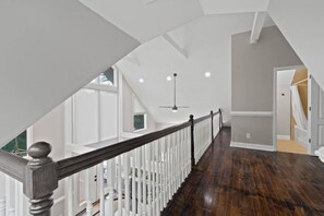 A spacious interior with a wooden staircase leading to a balcony, white railings, and a ceiling fan. - Etowah Overlook (Dahlonega)