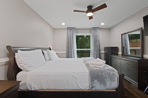 A bedroom with a bed, a ceiling fan, a dresser, and a window with curtains. - Etowah Overlook (Dahlonega)