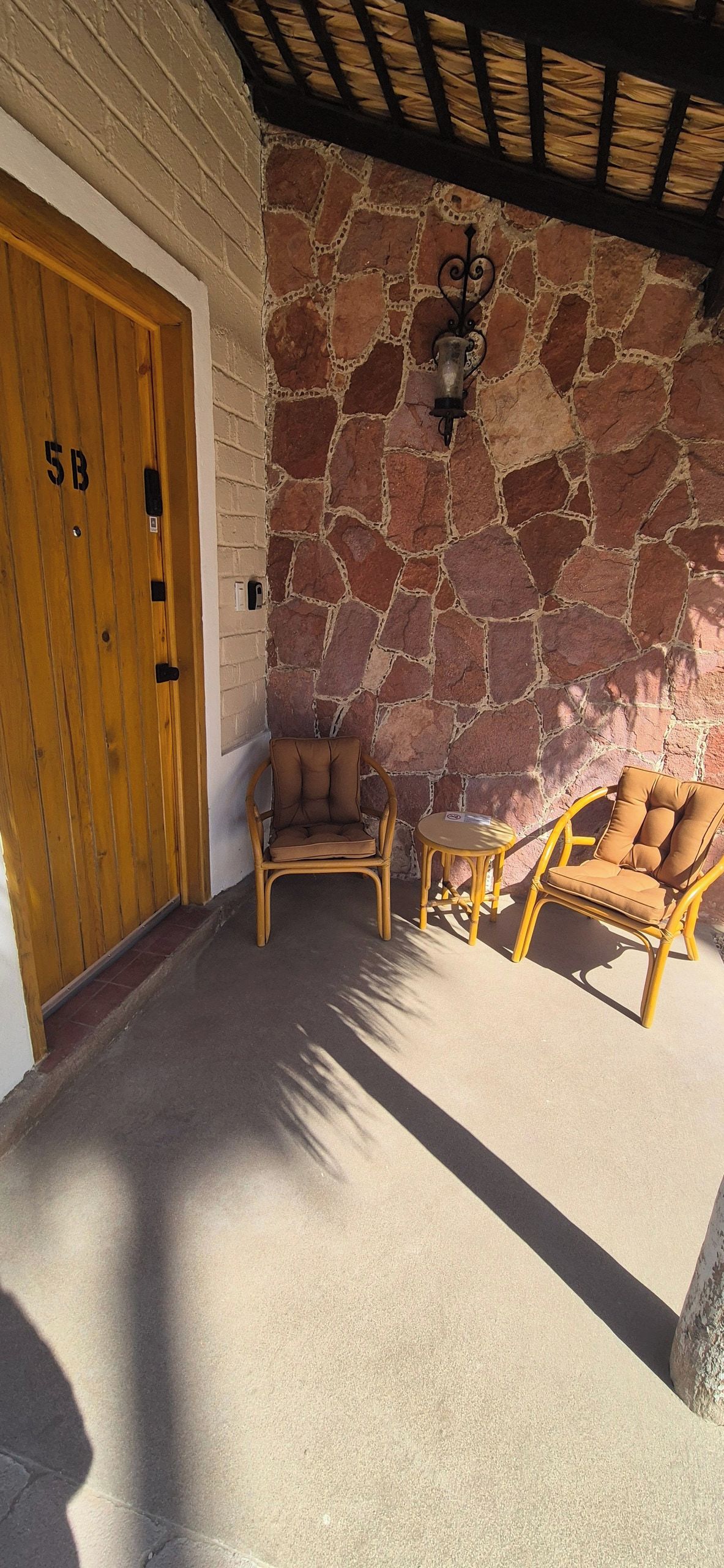 A room with a stone wall, a wooden door labeled '5B', two wicker chairs, and a small table.