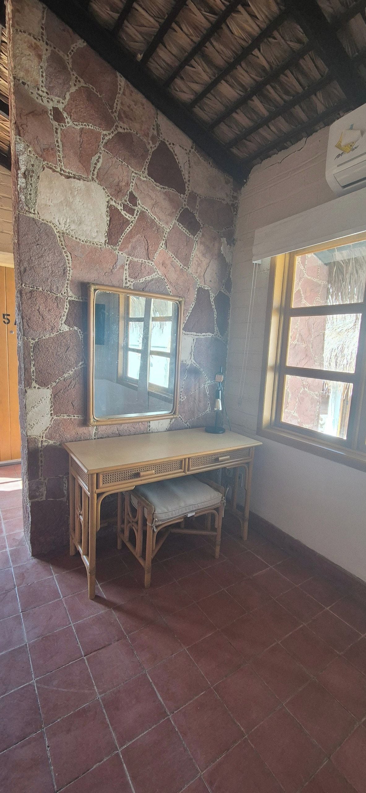 A room with a stone wall, a wooden desk, a chair, and a window.
