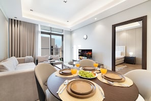A modern hotel room with a dining area, a sofa, a TV, and a bed. - 1BHK, Burj Khalifa View Business Bay (Dubai)