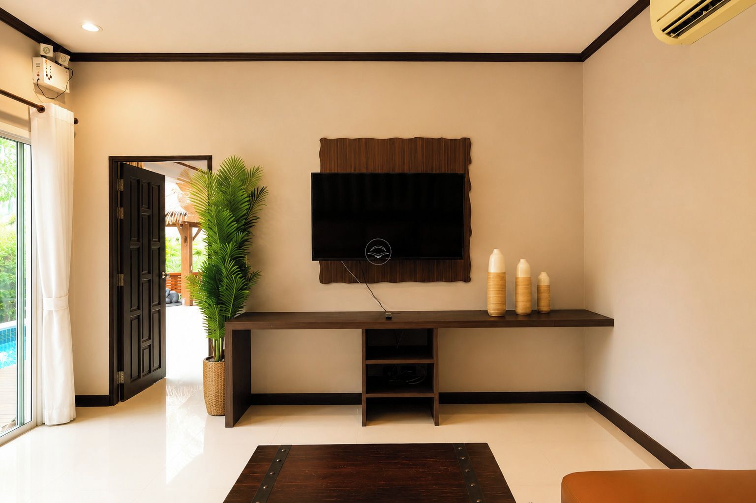 A modern living room with a flat-screen TV mounted on a wall, a wooden entertainment unit below, and a potted plant to the left.