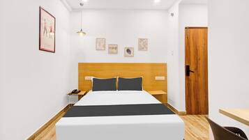 Quarto de hotel com cama, mesas de cabeceira, cabeceira de madeira, uma porta e uma parede decorada com quadros.