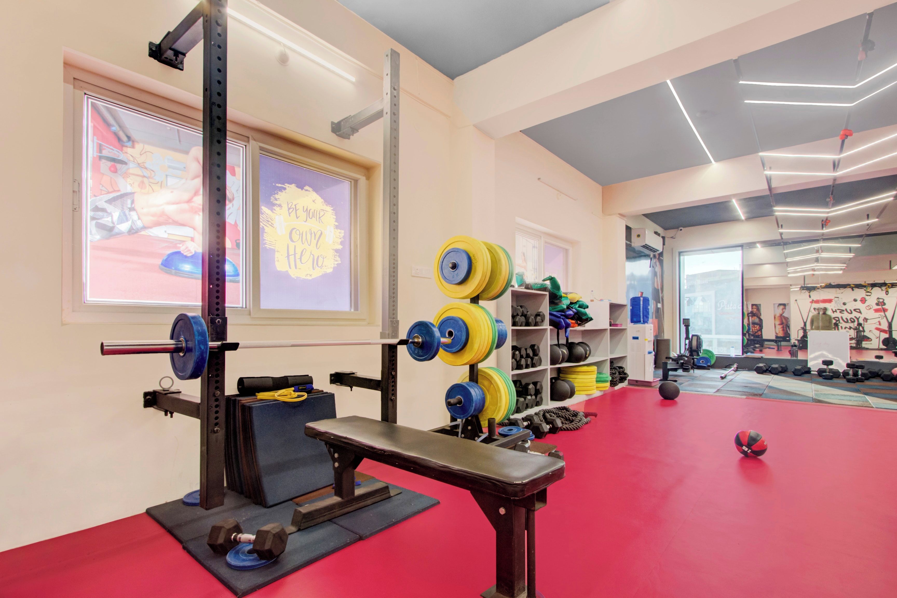 Un gimnasio con equipo de levantamiento de pesas, suelo rojo y carteles de motivación.