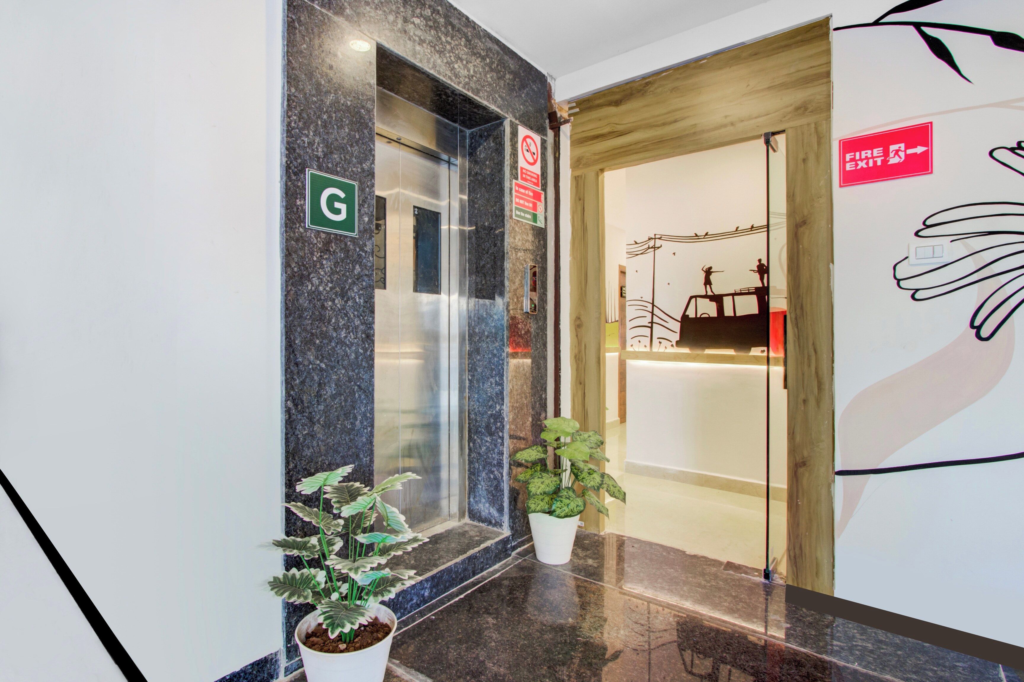 Um corredor interno com parede de mármore, um letreiro verde com a letra 'G', placa de saída de incêndio e um vaso de planta.