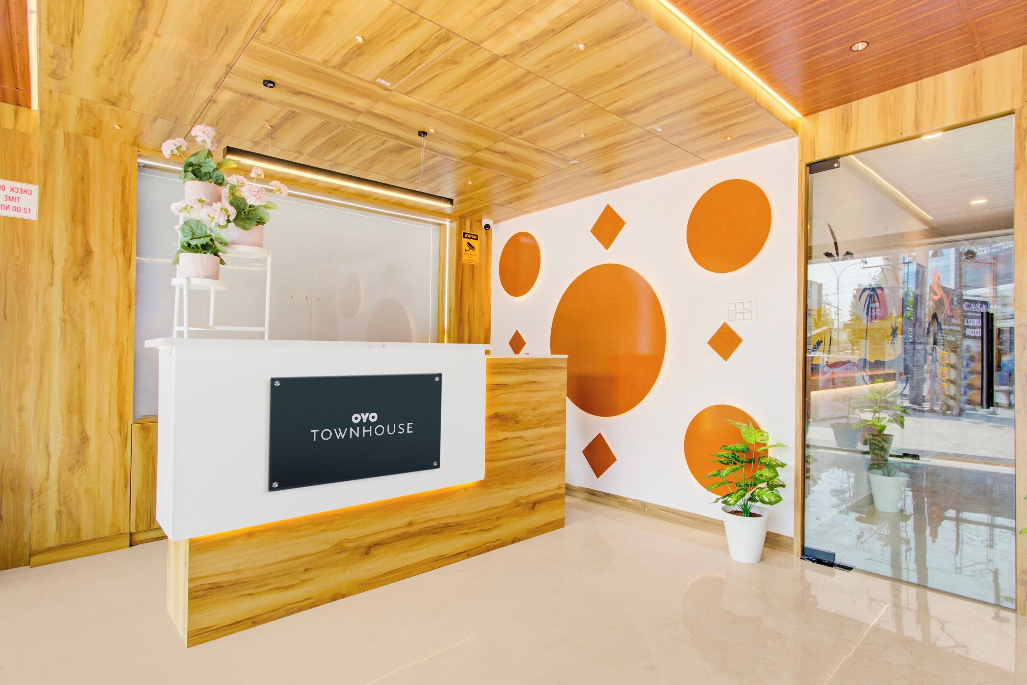 Een receptiebalie met een bord waarop 'OYO TOWNHOUSE' staat, in een modern interieur met houten lambrisering en geometrische wanddecoraties.