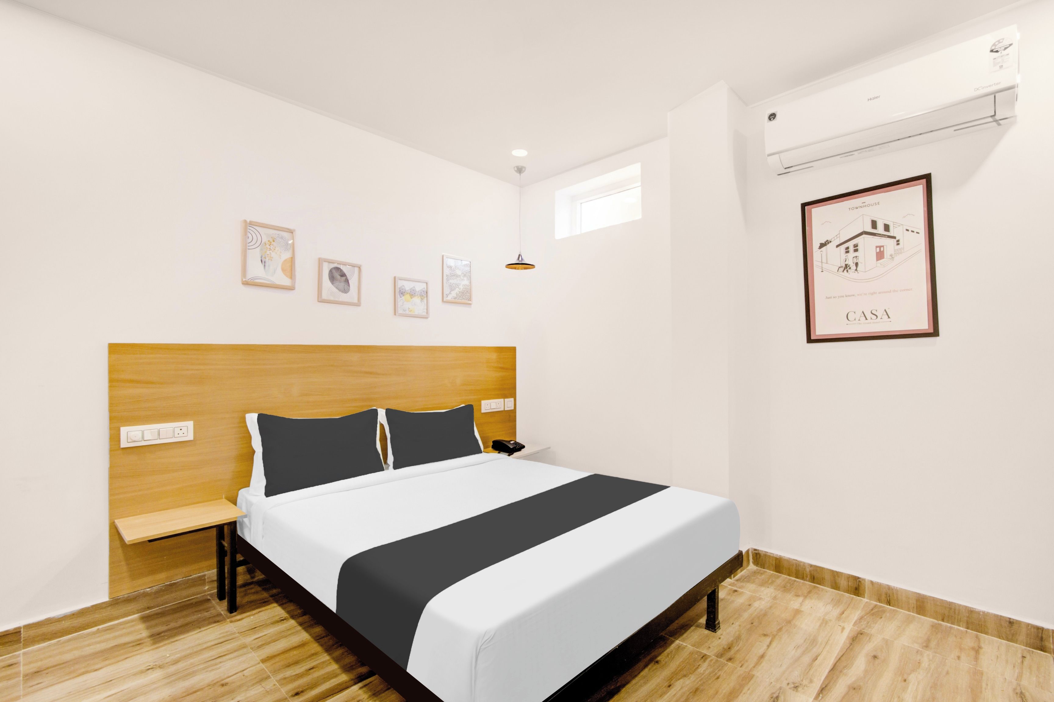 Una habitación de hotel con cama, cabecera de madera, ventana pequeña y un cuadro en la pared.