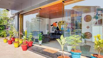 Um edifício moderno com entrada de vidro, plantas em vasos e uma área de estar com sofá e mesa.