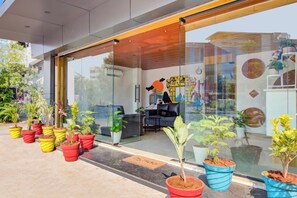 A modern building with a glass entrance, potted plants, and a seating area with a sofa and table. - Townhouse Casa Grand (Hanmakonda)