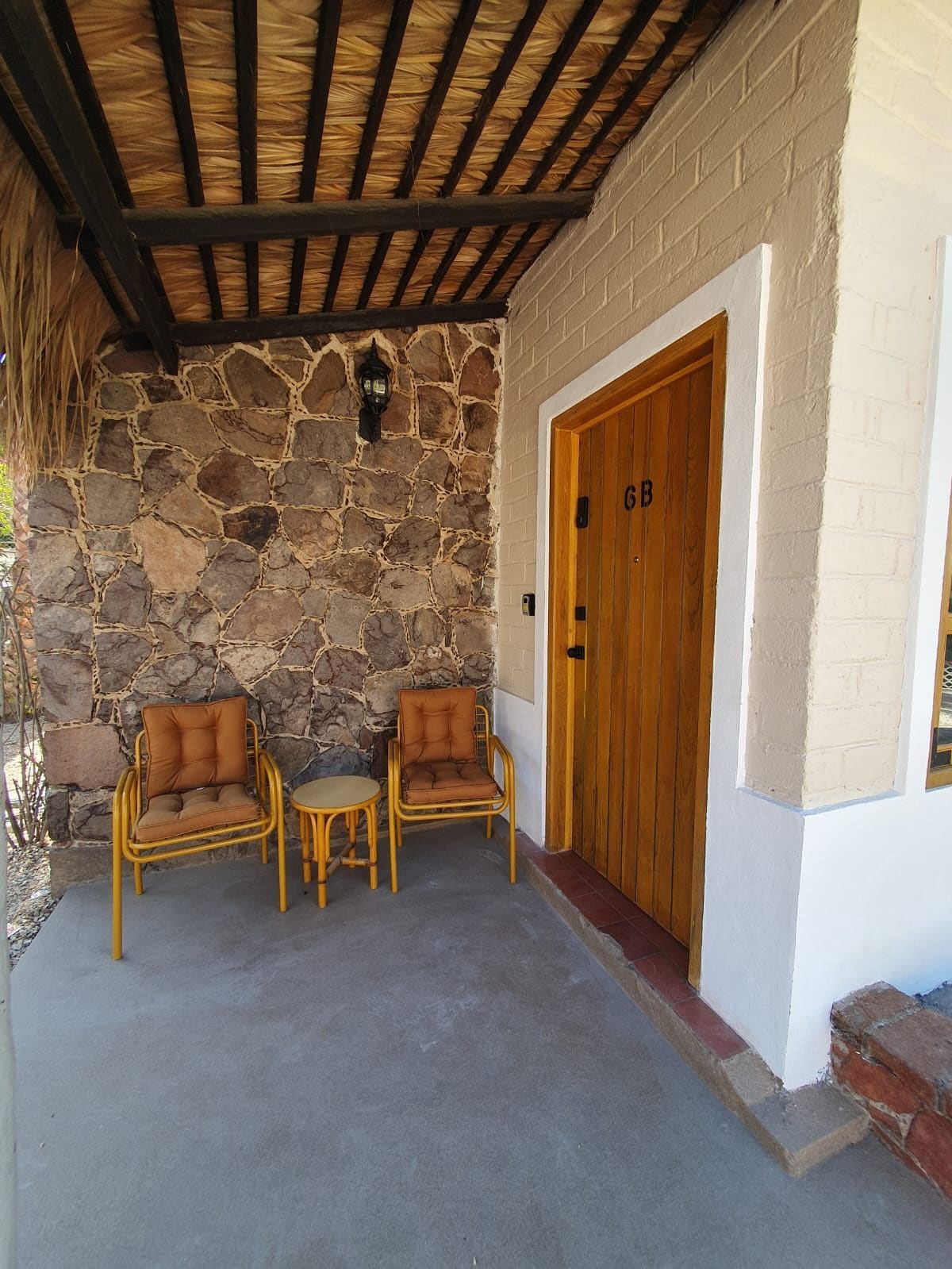 A covered outdoor seating area with stone walls and a wooden door marked 'GB'.