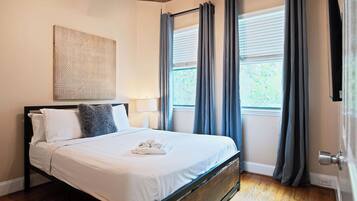 Une chambre à coucher avec un lit, une œuvre d’art accrochée au mur, une fenêtre avec des rideaux et une porte.