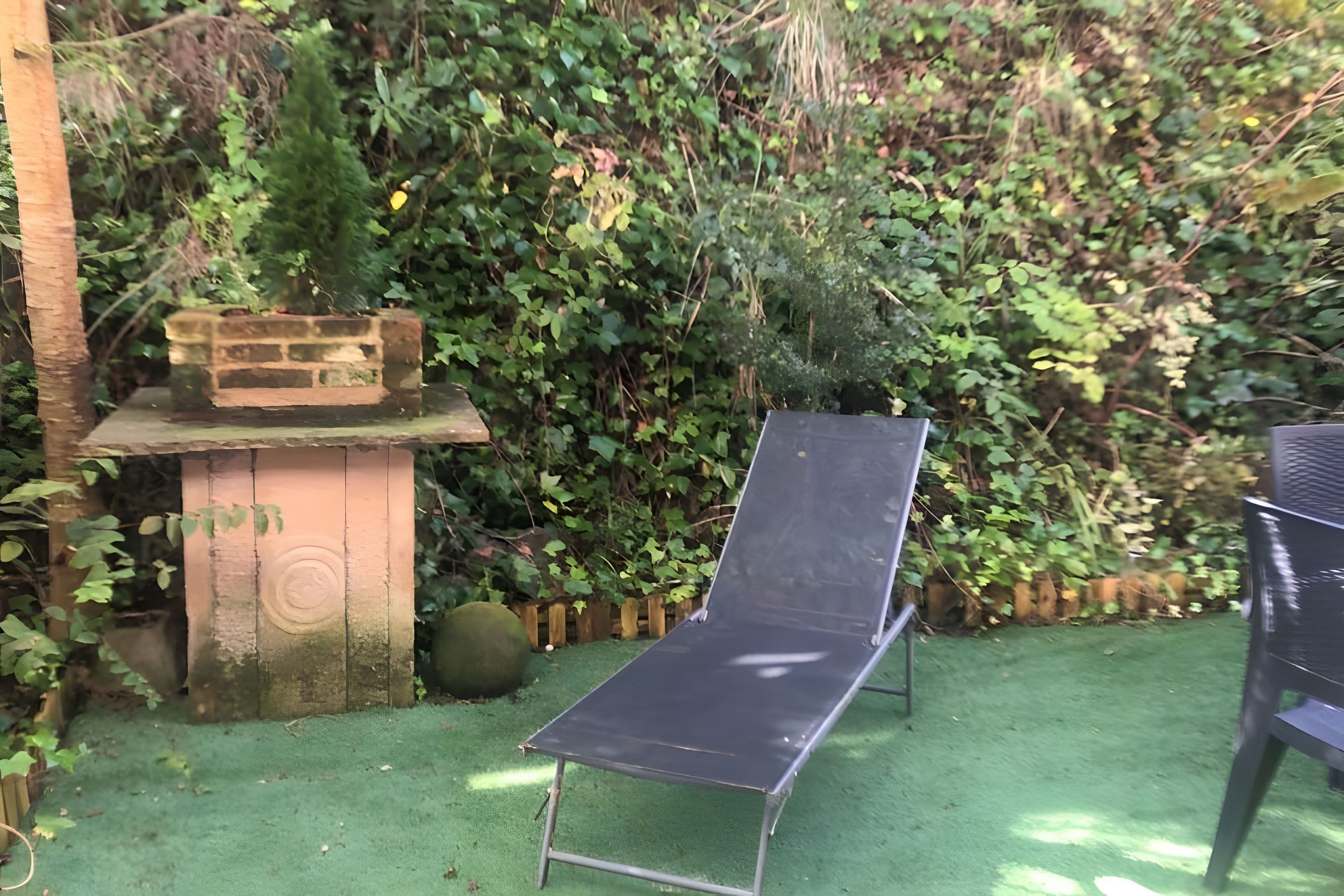 A garden with a metal chair, a brick planter, and dense foliage.