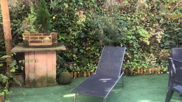 A garden with a metal chair, a brick planter, and dense foliage.