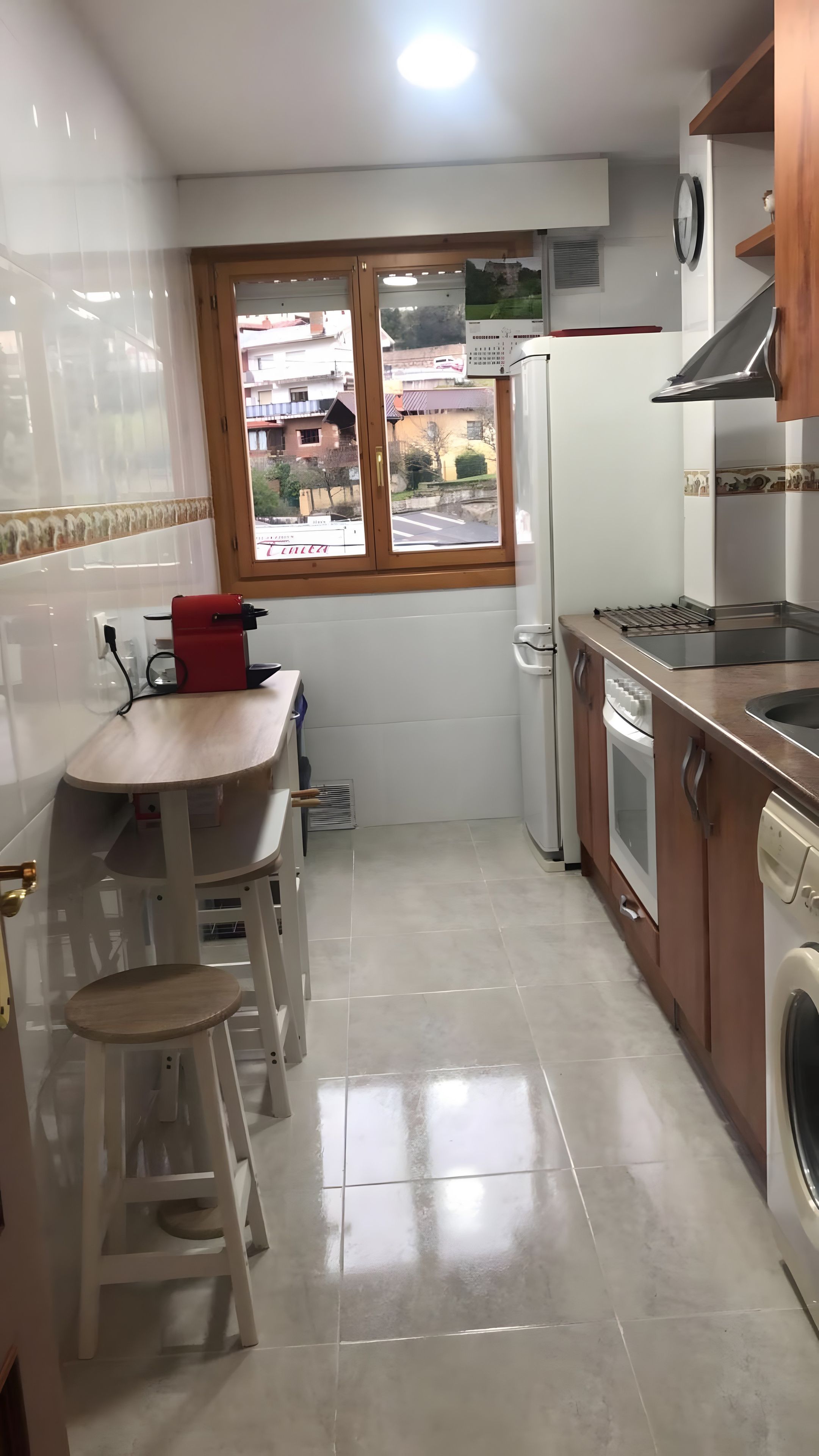Una cocina compacta con ventana, un lavamanos, lavadora y una pequeña mesa con taburetes.