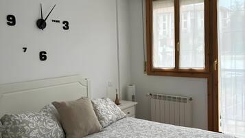 Un dormitorio con una cama, un reloj de pared, una ventana con cortinas y un radiador.