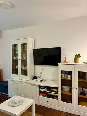 Uma sala de estar moderna com televisão de tela plana, armários brancos com portas de vidro e uma pequena mesa com um objeto decorativo.