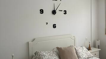 Un dormitorio con una cama blanca, una mesita de noche con una lámpara y un reloj de pared.