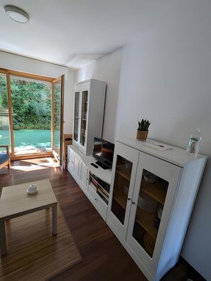 A modern kitchen with a built-in oven, a dining table, and a view of a garden through a glass door.