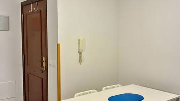 Un comedor con mesa blanca y sillas azules, una puerta de madera y una pared blanca con un interruptor de luz.