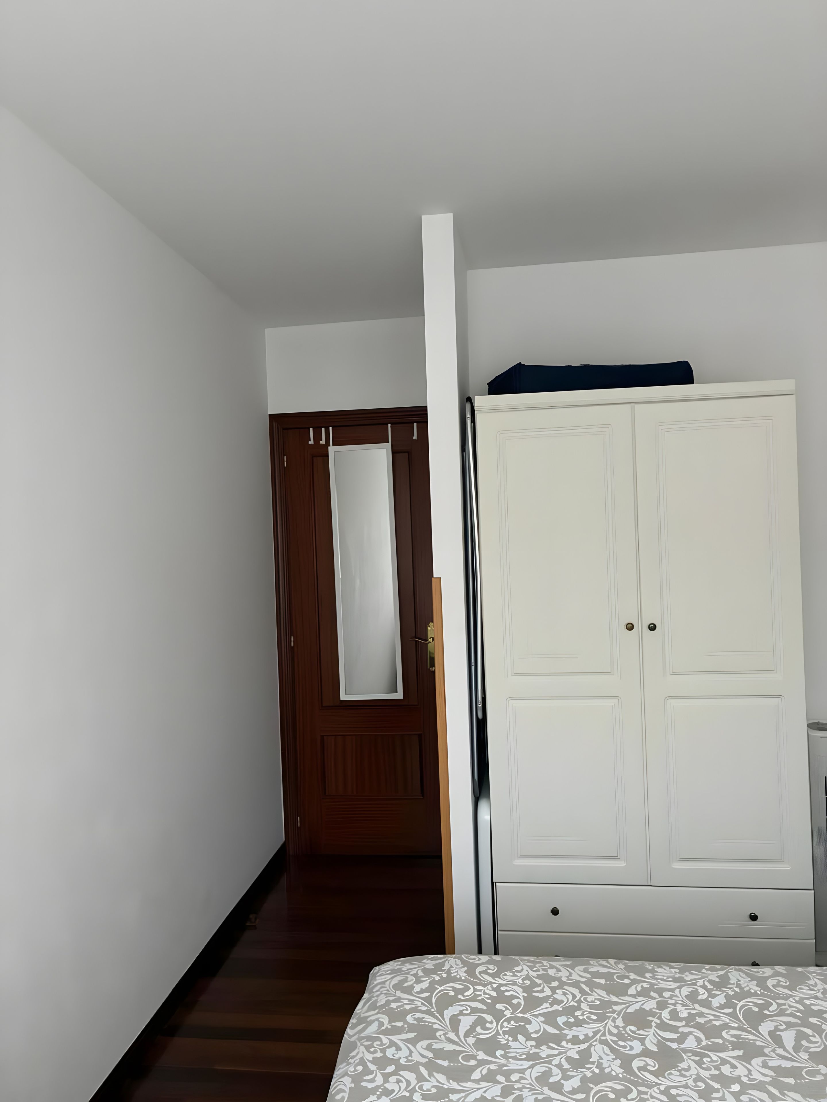 Une pièce avec une porte en bois, une armoire blanche et un lit recouvert d’une couvre-lit à motifs.