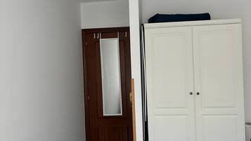 Una habitación con puerta de madera, un armario blanco y una cama con edredón estampado.