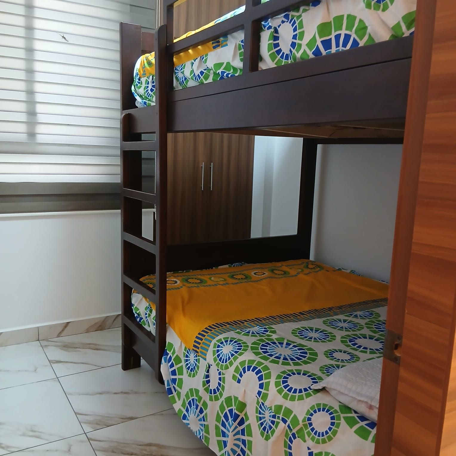 A bunk bed with a mirror, a shelf, and a patterned bedspread.
