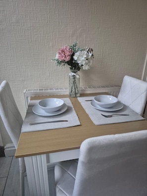 Een eettafel met twee witte borden, een vaas met bloemen en een witte stoel.