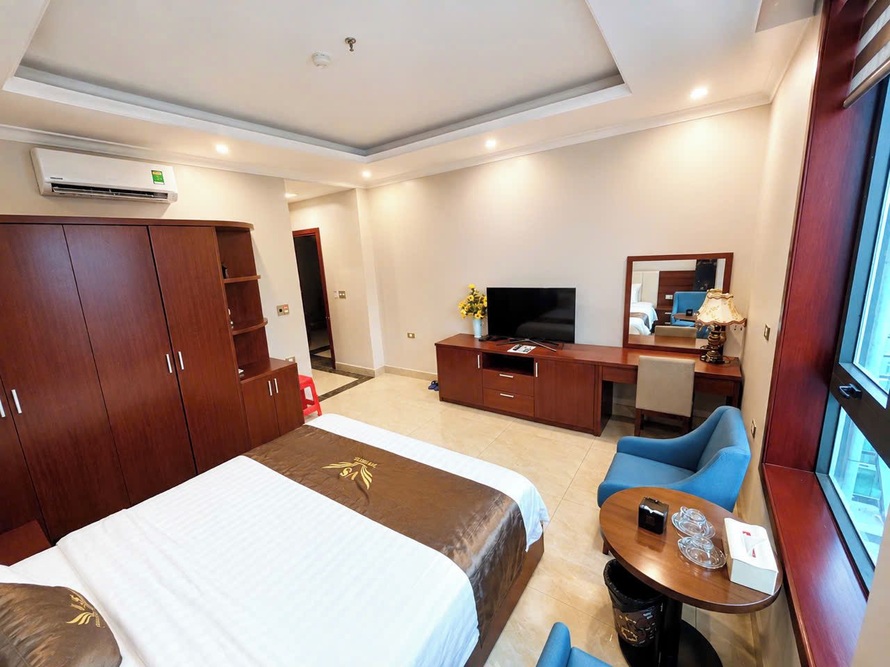 A hotel room with a bed, a desk, a chair, a TV, and a window.