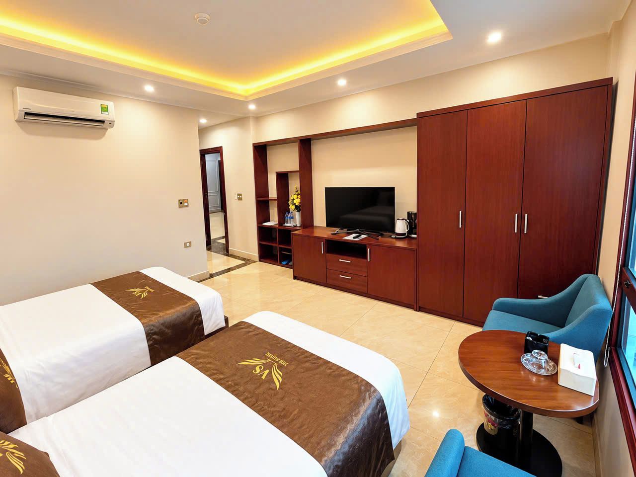 A hotel room with two beds, a TV, a desk, and a seating area.