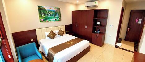 A hotel room with a bed, a blue armchair, a small table with a tray, a wardrobe, and a painting on the wall.