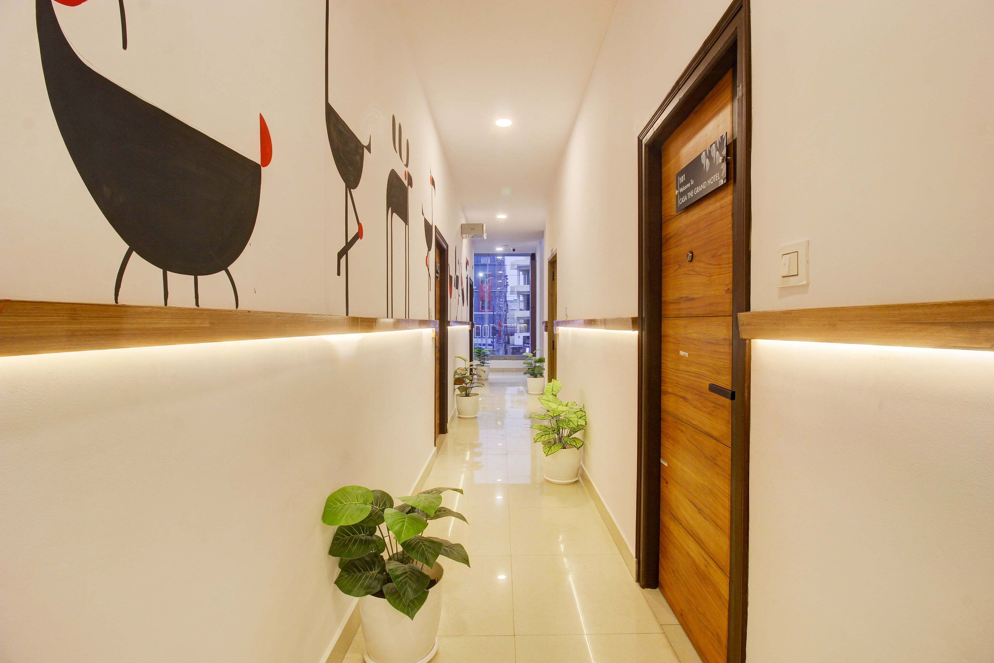 A hotel hallway with a reception desk, potted plants, and a sign indicating the location.