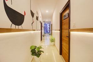 Corredor de hotel com balcão de recepção, plantas em vasos e placa indicando a localização.