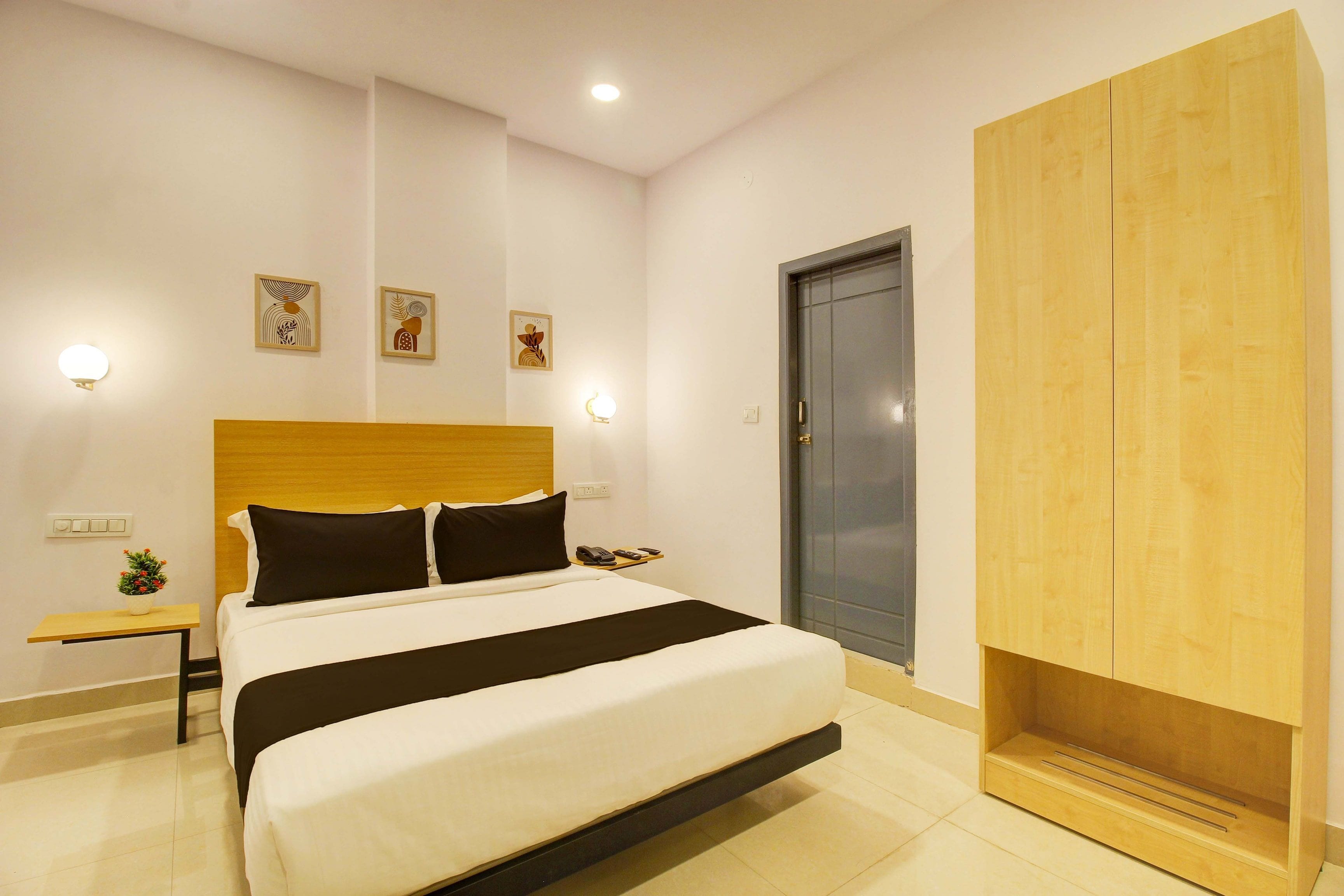 Una habitación de hotel con cama, mesitas de noche, armario y cuadros colgados en la pared.