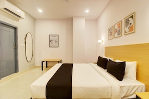 Quarto de hotel com cama, escrivaninha, cadeira, porta e ar-condicionado fixado na parede.