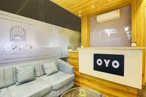 A reception area with a couch, a wooden reception desk, and a wall with a logo and text. - Collection O Casa Grand Hotels Nacharam (Hyderabad)
