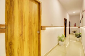 A hotel corridor with a wooden door, white walls, and potted plants. - Collection O Casa Grand Hotels Nacharam (Hyderabad)