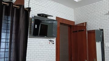 Una habitación con paredes de ladrillo blanco, un ventilador de techo, un equipo de aire acondicionado, una puerta de madera y una ventana con cortina.