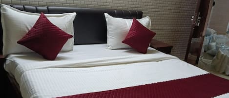 Ein Bett mit Kopfteil, zwei Kissen und einer roten Decke in einem Raum mit einer Ziegelwand.