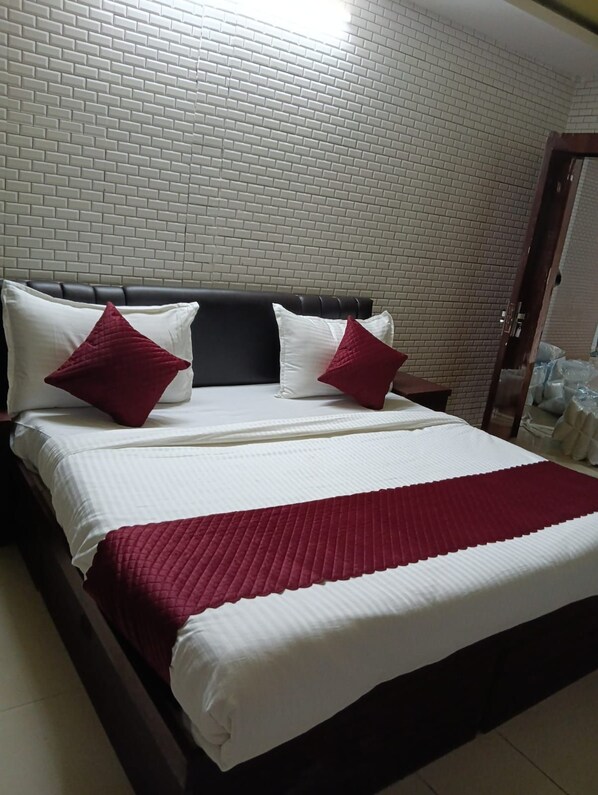 A bed with a headboard, two pillows, and a red blanket in a room with a brick-patterned wall. - HOTEL N-3 (Kota)