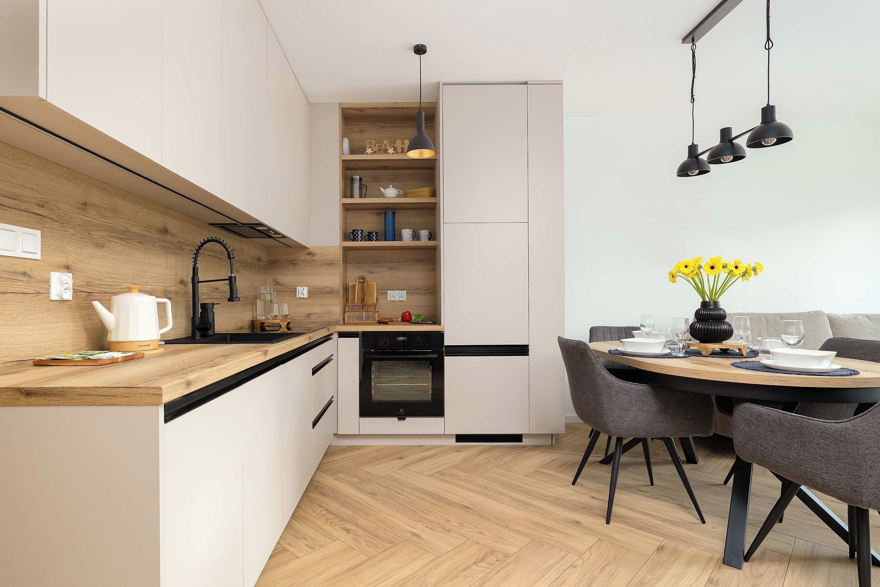 A modern kitchen with a built-in oven, a dining area with a table set for two, and a hanging light fixture above the table.