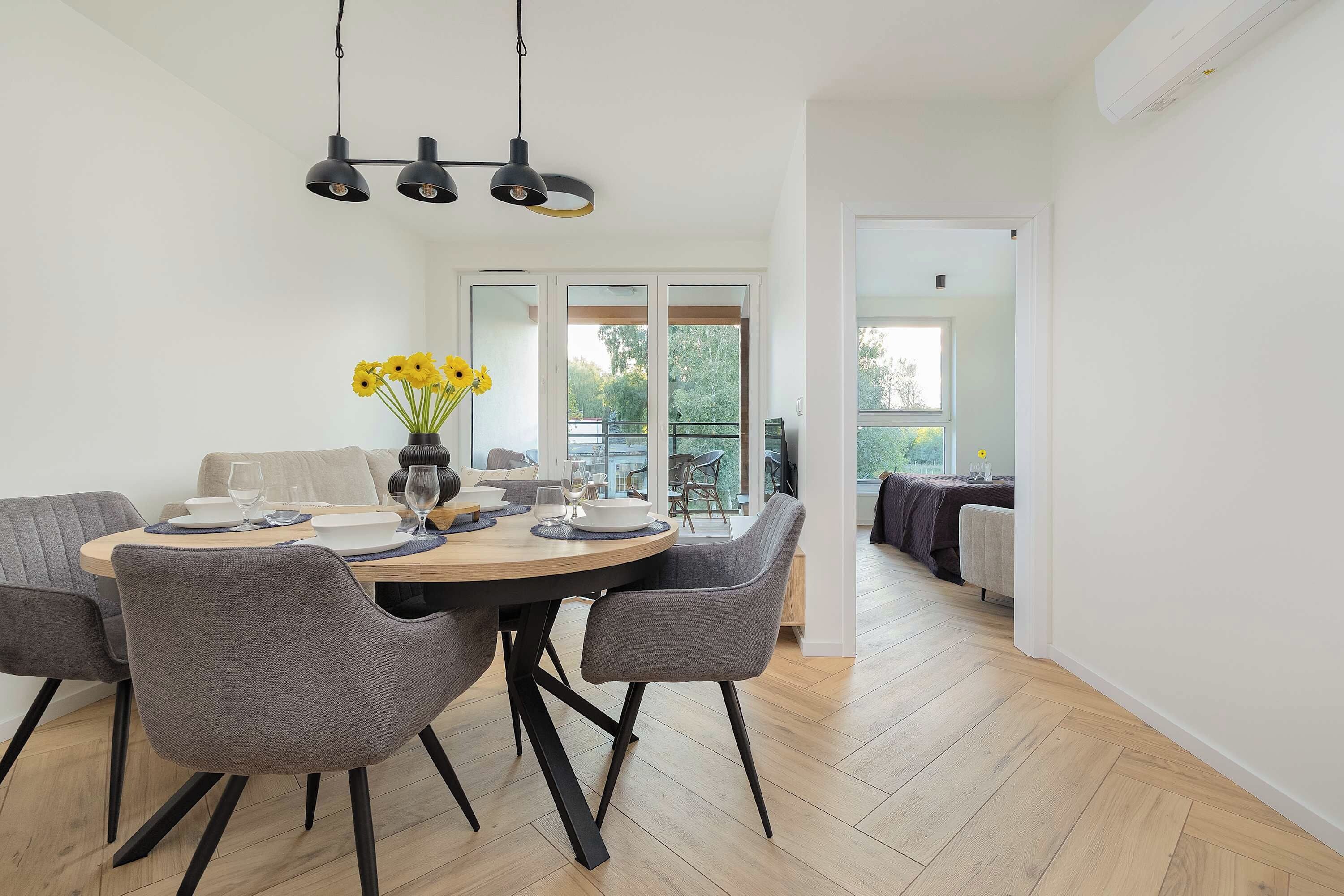 A dining area with a round table, grey upholstered chairs, and a vase with yellow flowers.