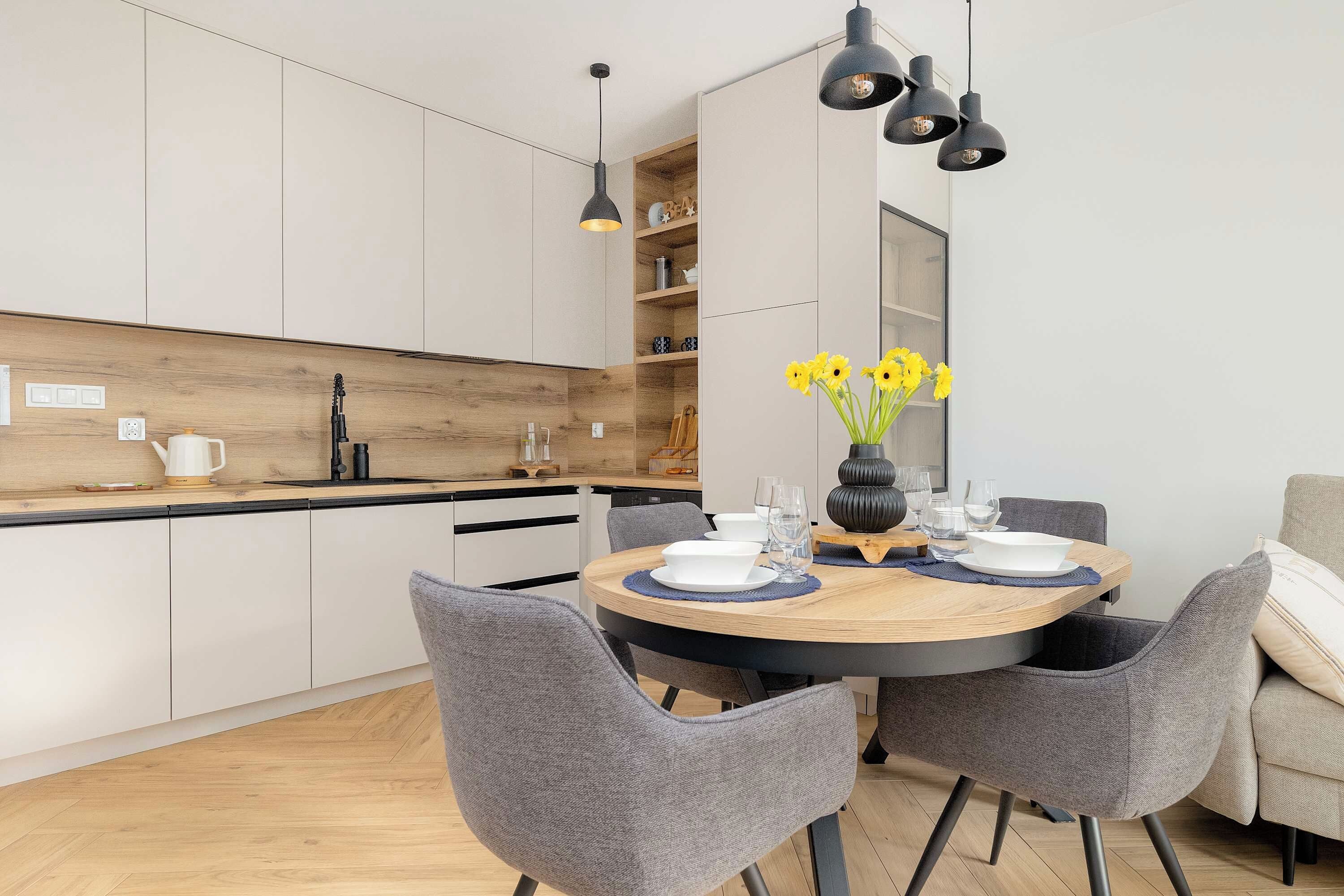 Una cocina moderna con armarios blancos, encimera de madera y una zona de comedor con una mesa redonda para cuatro.