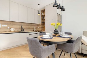 Una cocina moderna con armarios blancos, encimera de madera y una zona de comedor con una mesa redonda para cuatro.