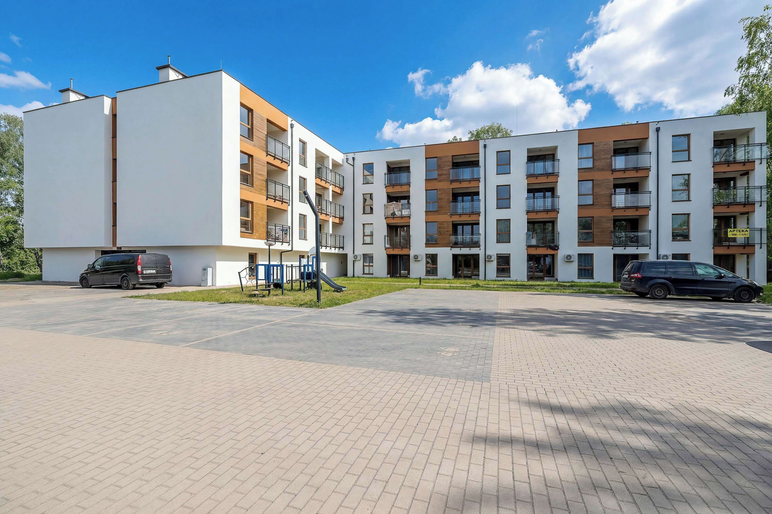 A modern apartment building with multiple balconies, a playground, and a paved parking area.